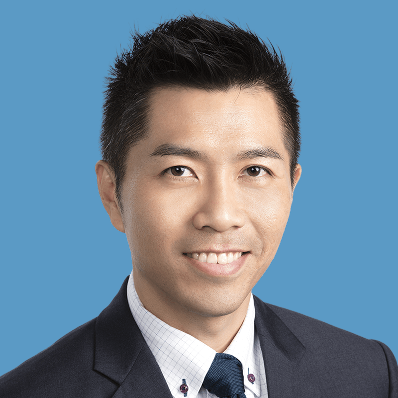 Headshot of Raymond Liow, a smiling Asian man in a dark suit against a blue background.